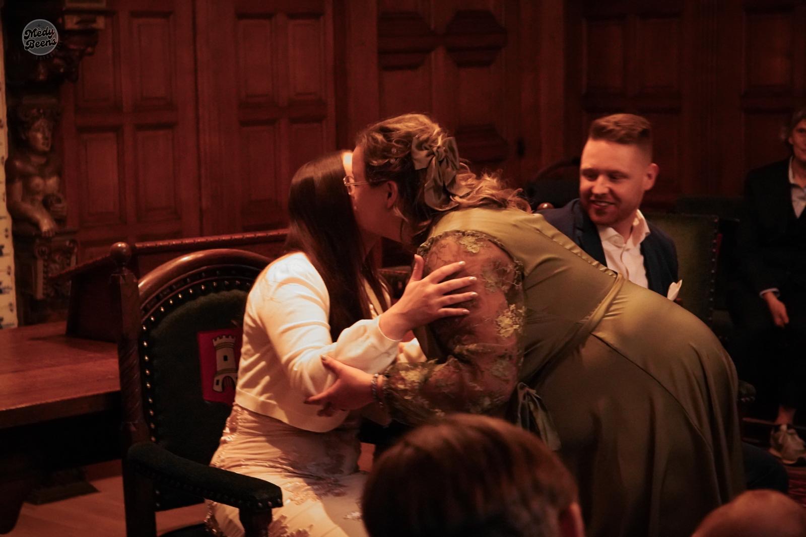 Marinda omhelst een bruid tijdens de ceremonie, terwijl haar partner toekijkt.